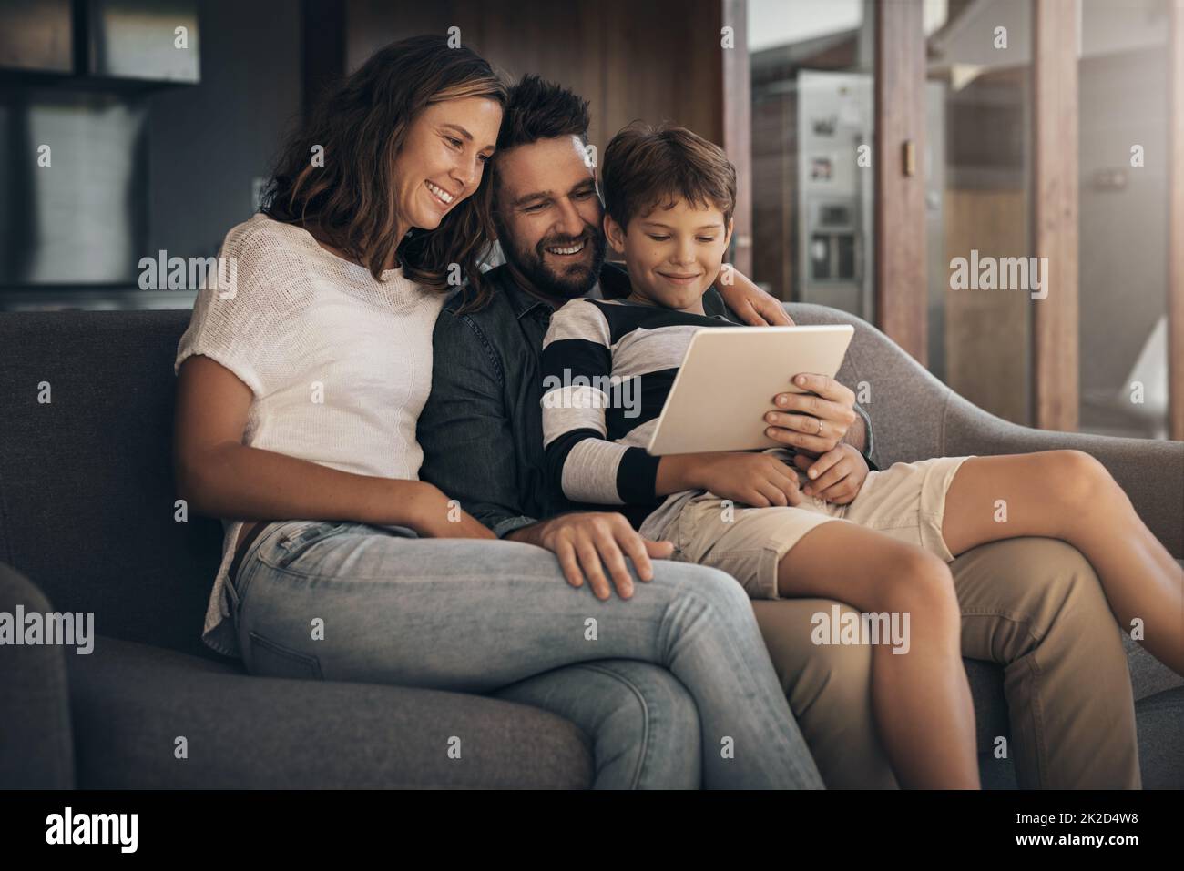 Share the love, share the fun. Shot of an adorable little boy using a digital tablet with his mother and father on the sofa at home. Stock Photo