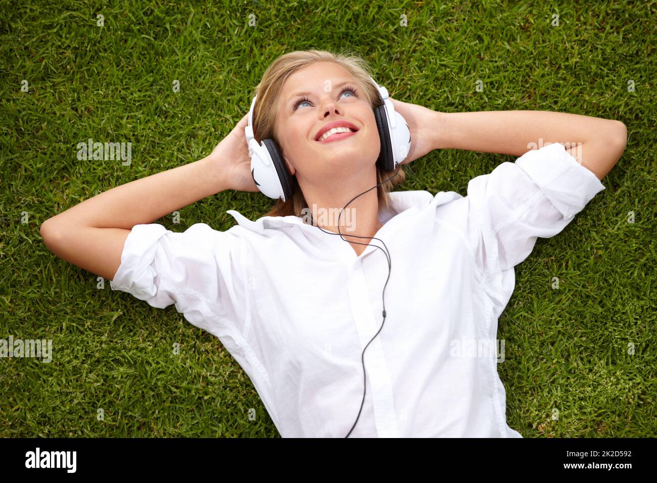 Getting lost in the music. High angle shot of a woman lying on a grassy field listening to musicHigh angle shot of a woman lying on a grassy field listening to music with her eyes closed. Stock Photo