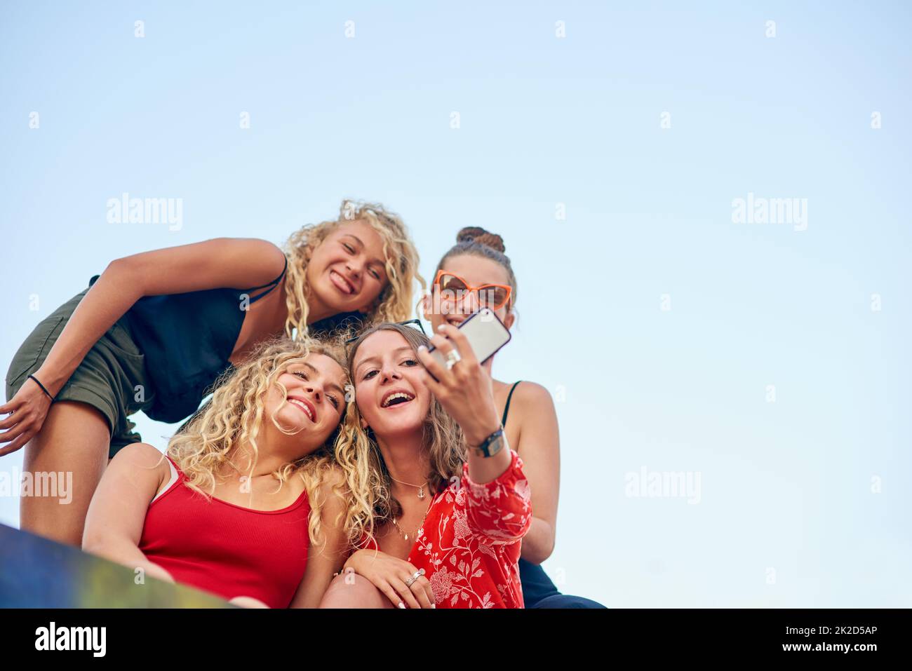 Its all about the angle. Low angle shot of a group of attractive young girlfriends taking selfies in the city. Stock Photo