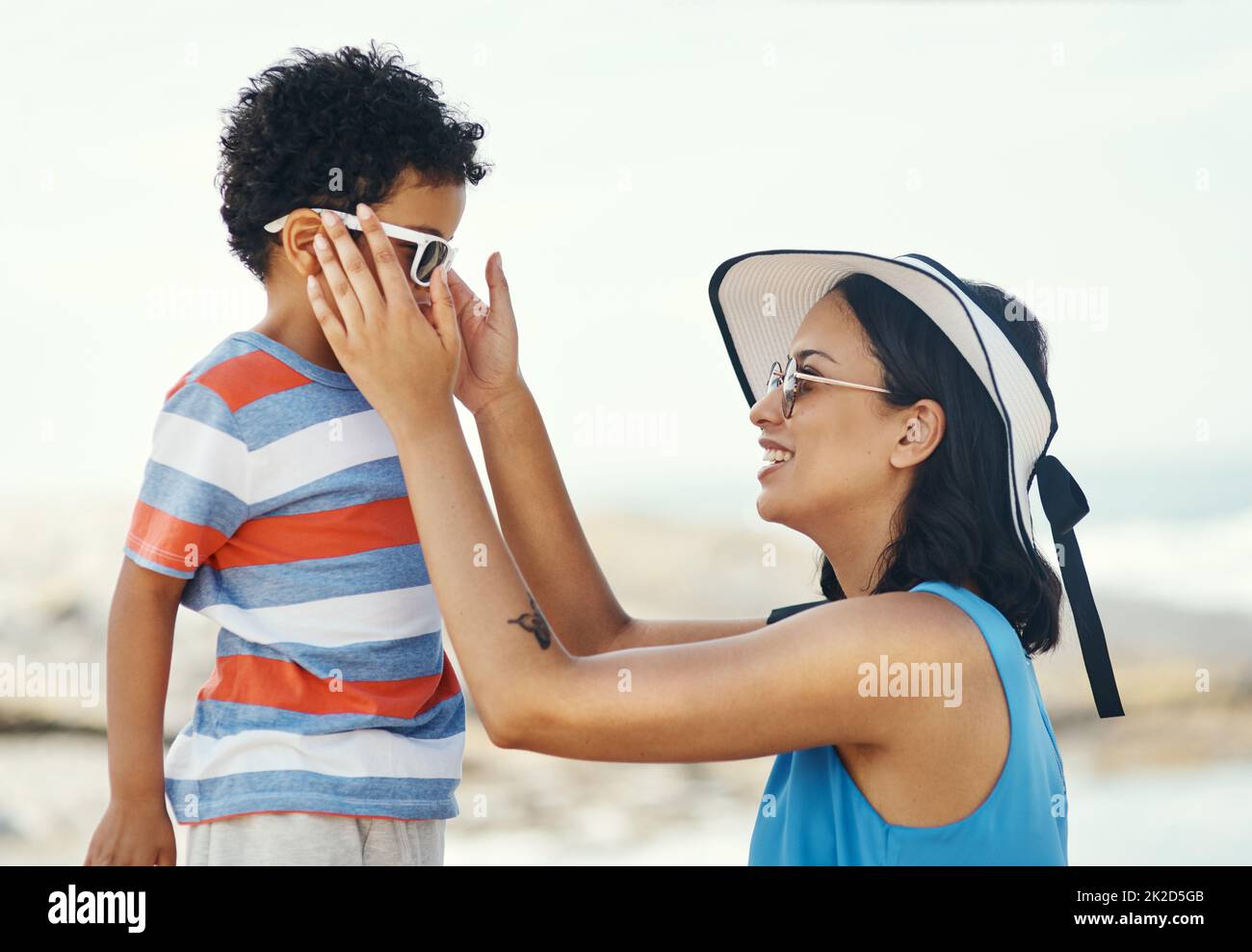 Sunglasses are really helpful for protecting your eyes. Shot of a mother applying sunscreen to her son at the beach. Stock Photo