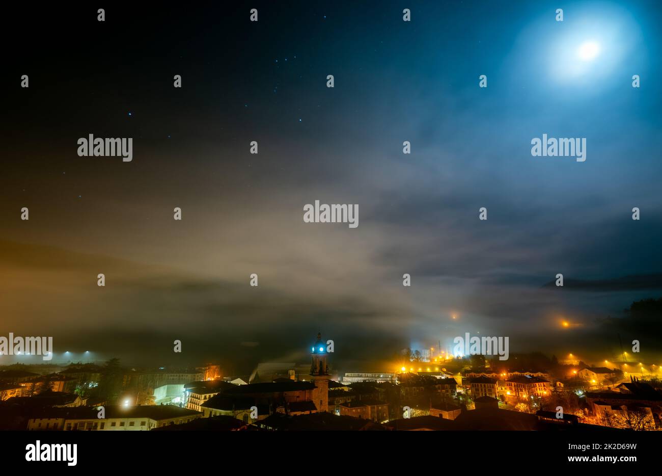 Cityscape in the night with stars in the sky. City in mist. Europe building in mist. City and orange light in the night. City covered with fog. Foggy sky. Old town in Europe. Picturesque cityscape. Stock Photo