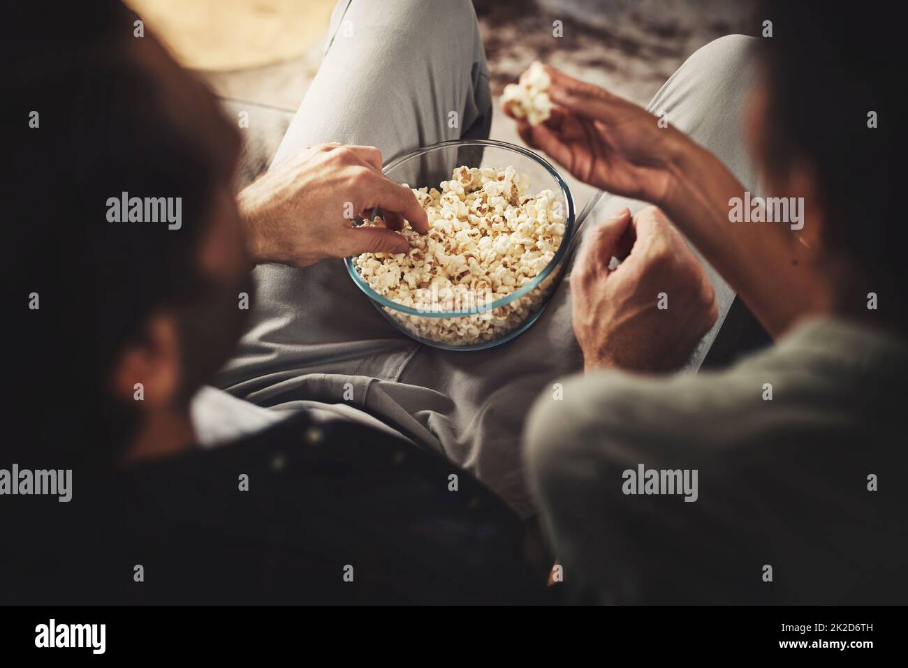 Gotta be love if Im sharing popcorn. Rearview shot of a young couple sitting on sofa snacking on popcorn together at home. Stock Photo