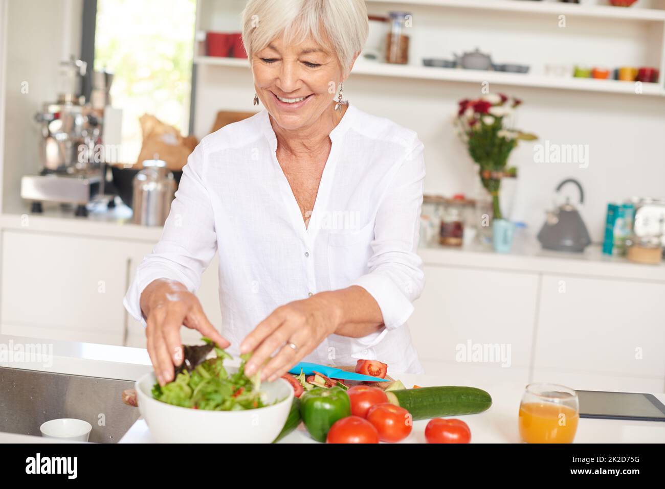 The secret to vitality is a healthy diet. Shot of a senior woman making a salad in her kitchen. Stock Photo