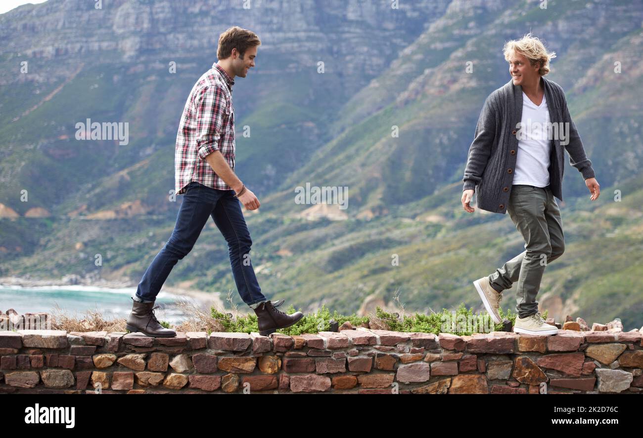 Bonding with my buddy outdoors. Shot of two young men walking on a stone wall with the mountain in the background. Stock Photo