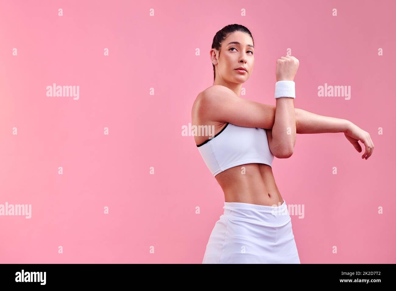Making excuses will get you nowhere. Studio shot of a sporty young woman stretching her arms against a pink background. Stock Photo