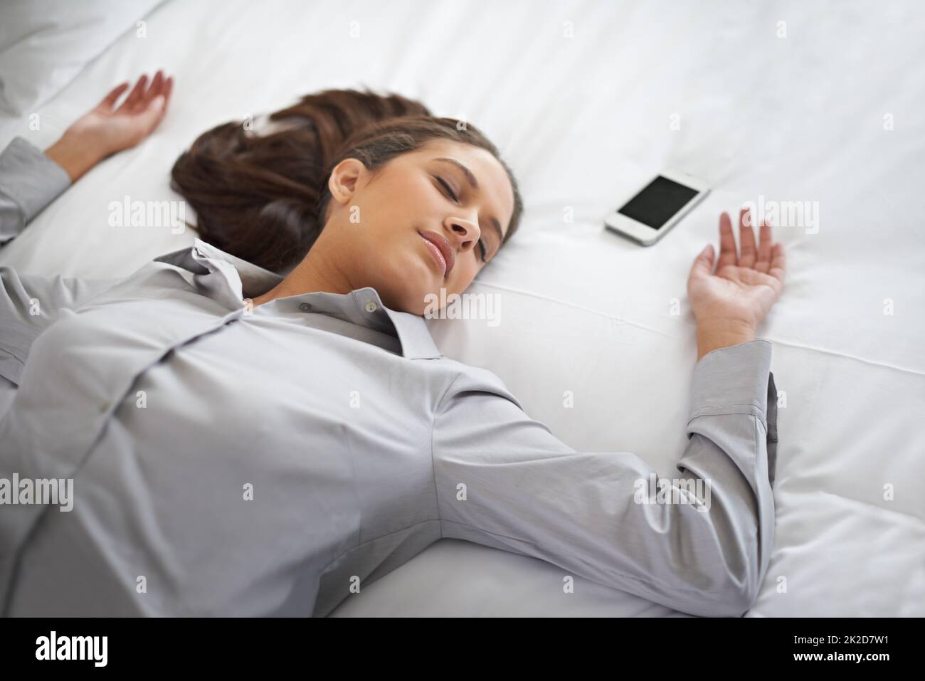 No more work today. Shot of a young businesswoman passed out on a bed with her cellphone beside here. Stock Photo