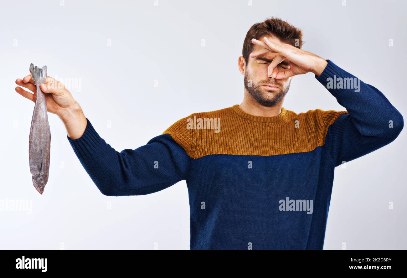 Stings the nostrils....yuck. Studio shot of a man showing disgust while holding a smelly fish. Stock Photo