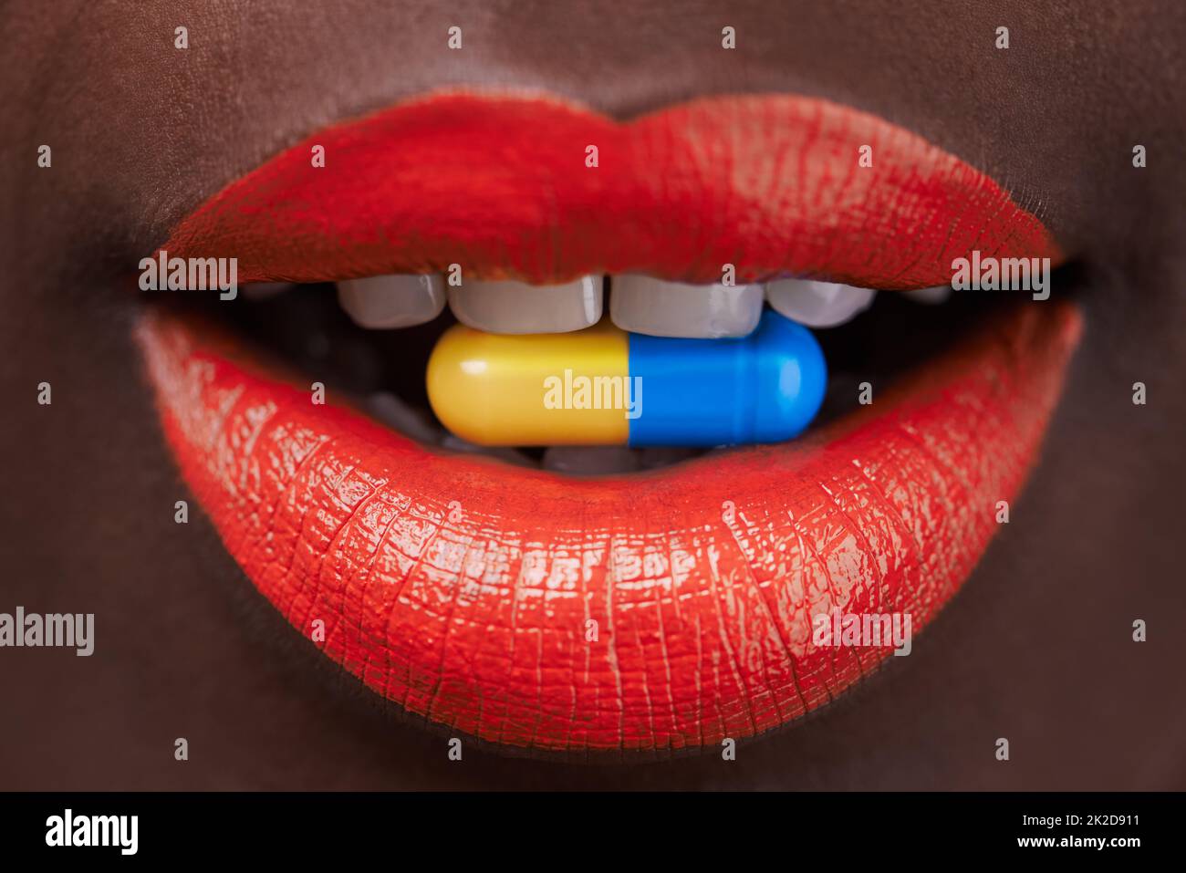 Taking a trip. Cropped view of an african woman with bright red lips with a capsule in her mouth. Stock Photo