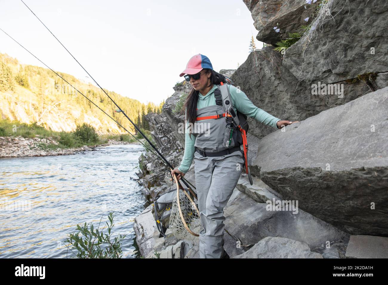 Woman carrying fishing rods on rocks Stock Photo