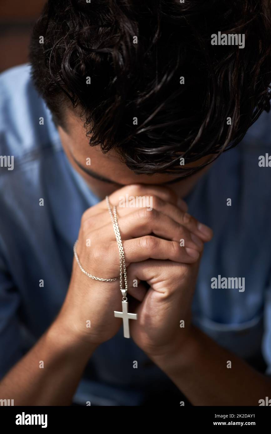 Praying for an answer. A young man bowing his head and holding a crucifix. Stock Photo
