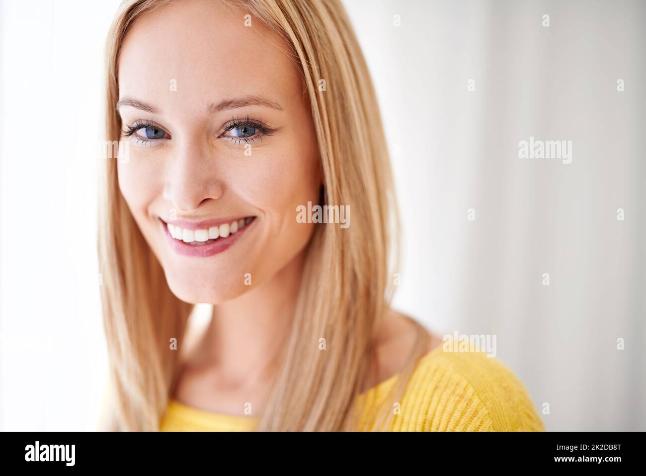 I smile because I have no idea whats going on. A young woman standing in her home smiling happily. Stock Photo
