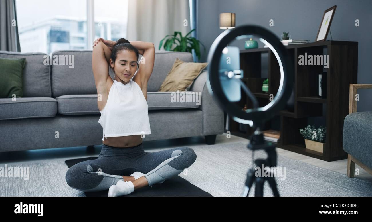 Grab your yoga mat and join me for a virtual session. Shot of a woman recording herself with a ring light and her cellphone while exercising at home. Stock Photo