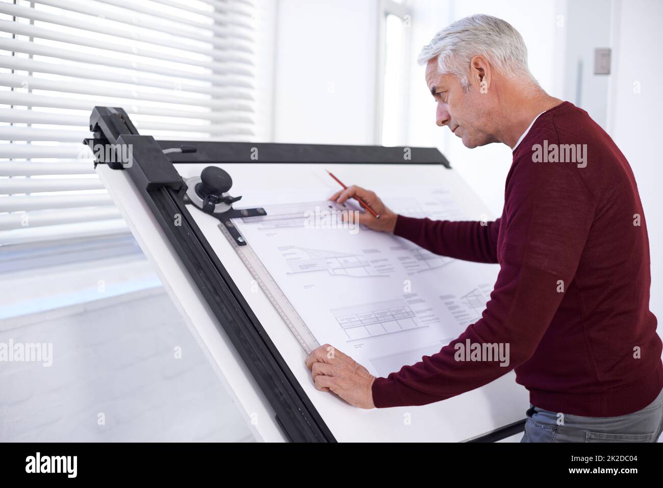 Doing what he does best. Cropped shot of a male architect working on a building plan at a drawing board. Stock Photo