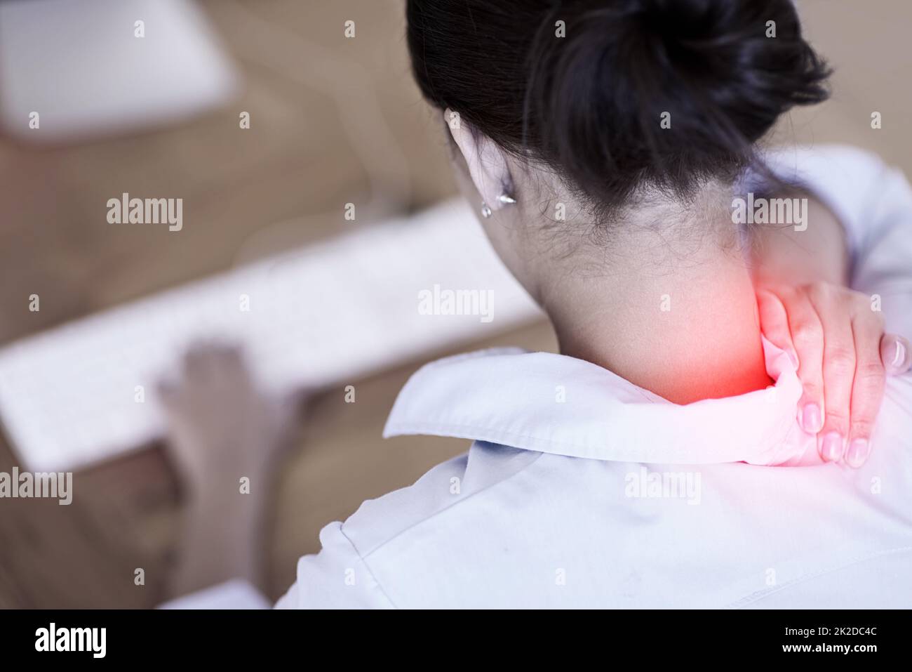 Sometimes work can be a pain in the neck. Rearview shot of a businesswoman at her computer holding her aching neck, highlighted in red. Stock Photo