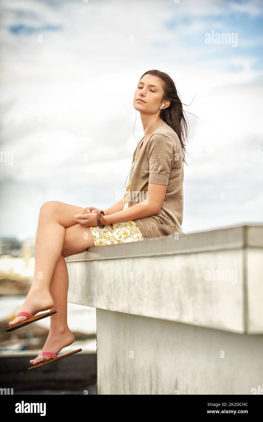 Enjoying the moment. Pretty young woman listening to music while sitting on a rooftop. Stock Photo