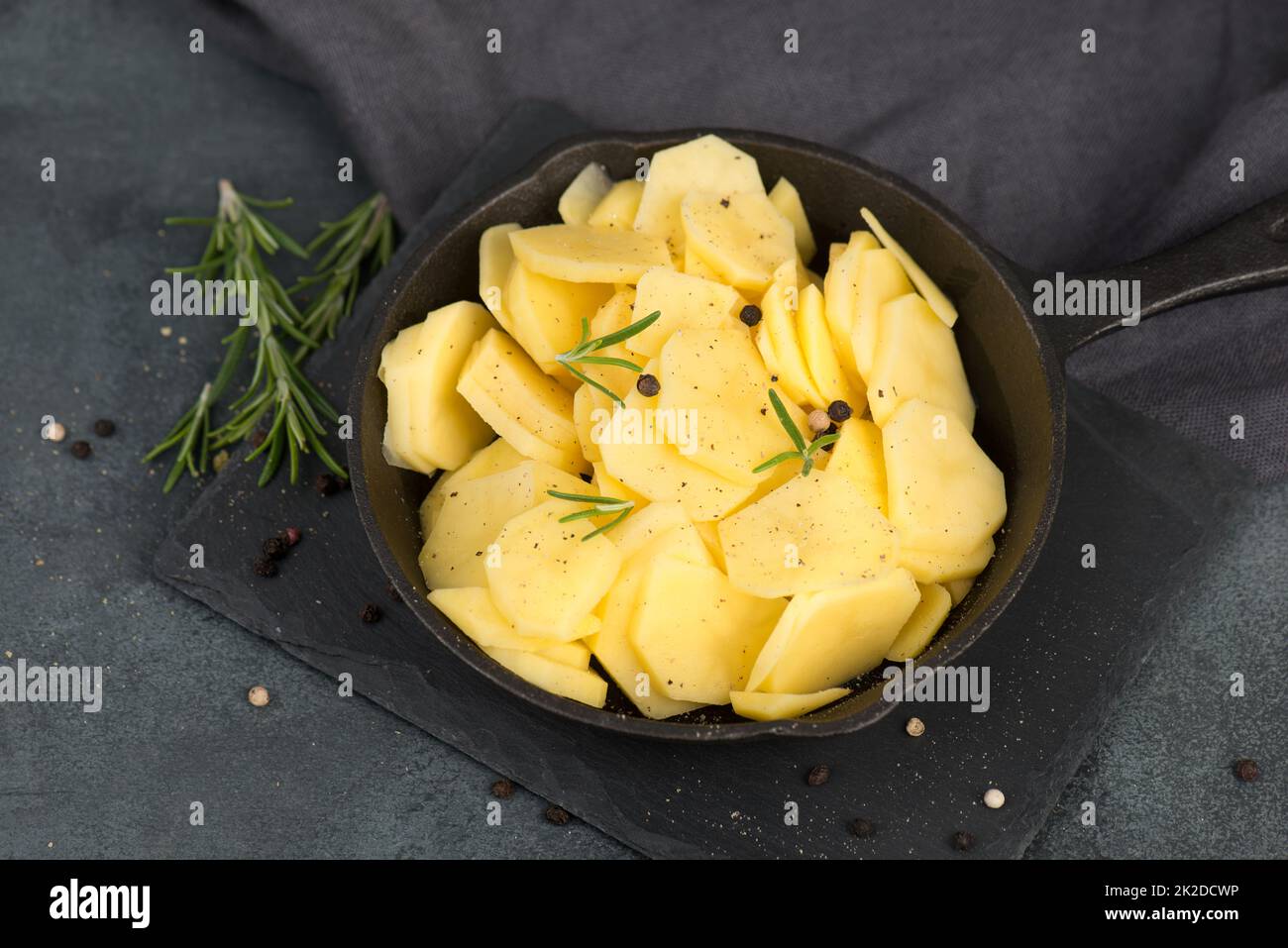 Sliced potatoes in a pan with rosmarine, pepper and olive oil, healthy vegetarian food Stock Photo