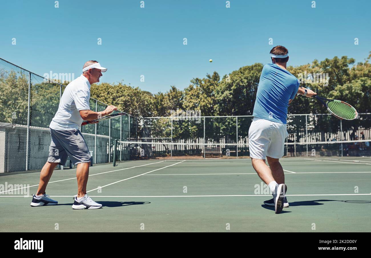 Work on that swing. Full length shot of a handsome mature sportsman coaching a fellow team-mate during a tennis training session. Stock Photo