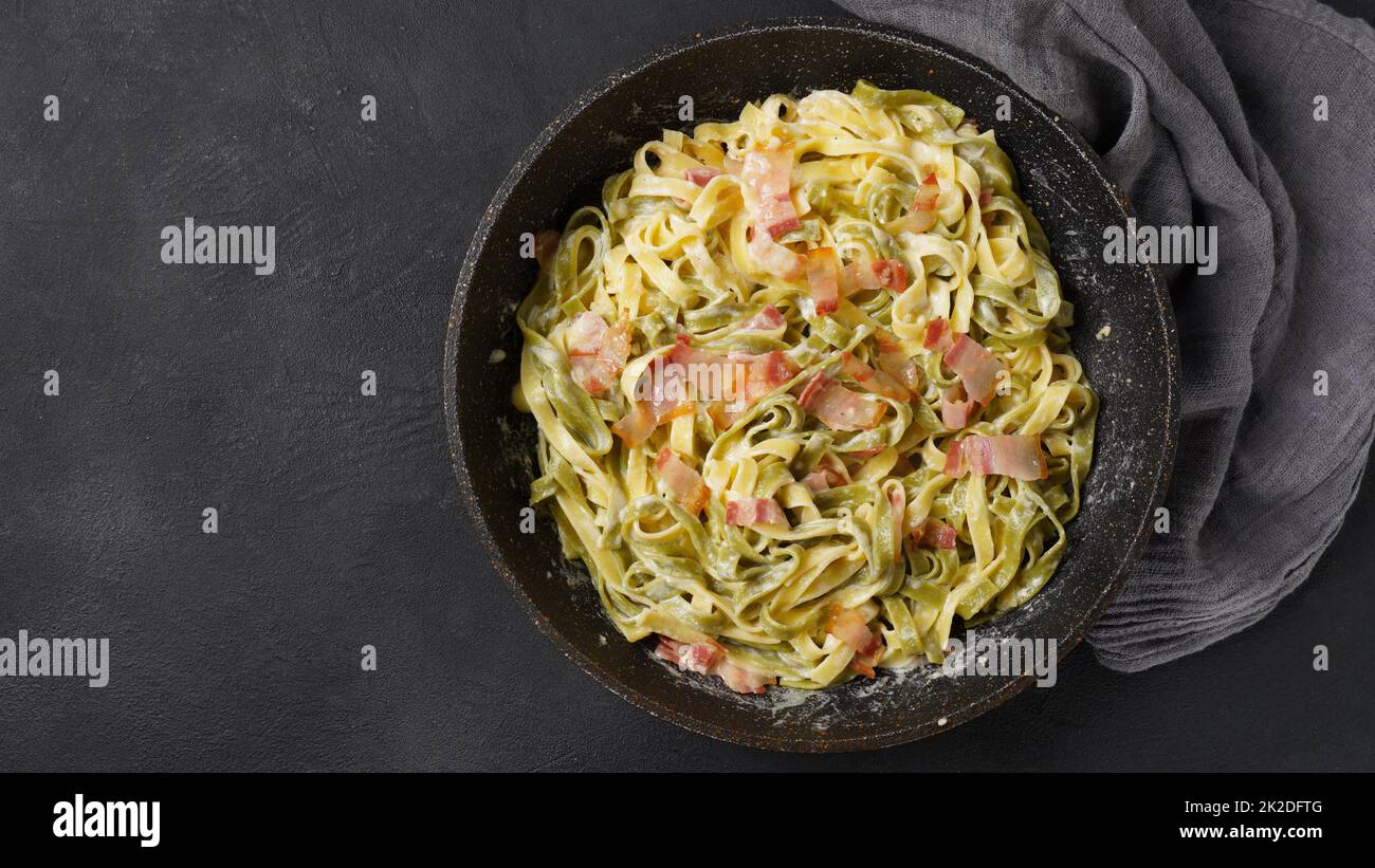 Italian egg pasta carbonara in black pan with bacon, parmesan cheese