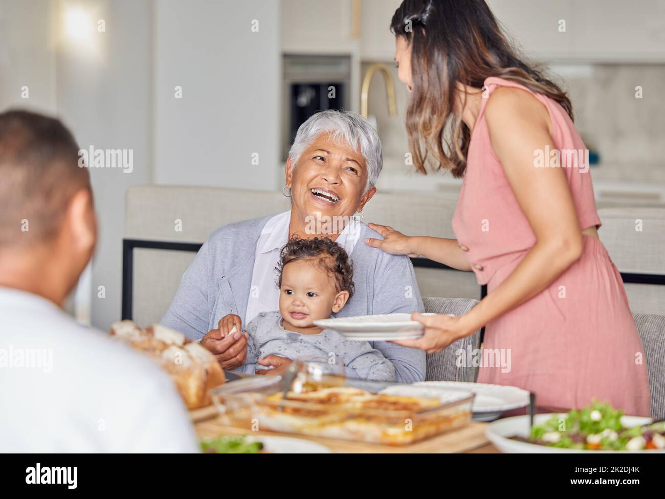 Family, grandmother and baby with food at the dining room or kitchen table for mothers day. Happy mother, father and grandma playing with newborn Stock Photo