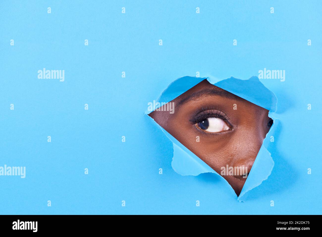 Is there something there. A view of a womans eye looking through a hole in some colorful paper. Stock Photo