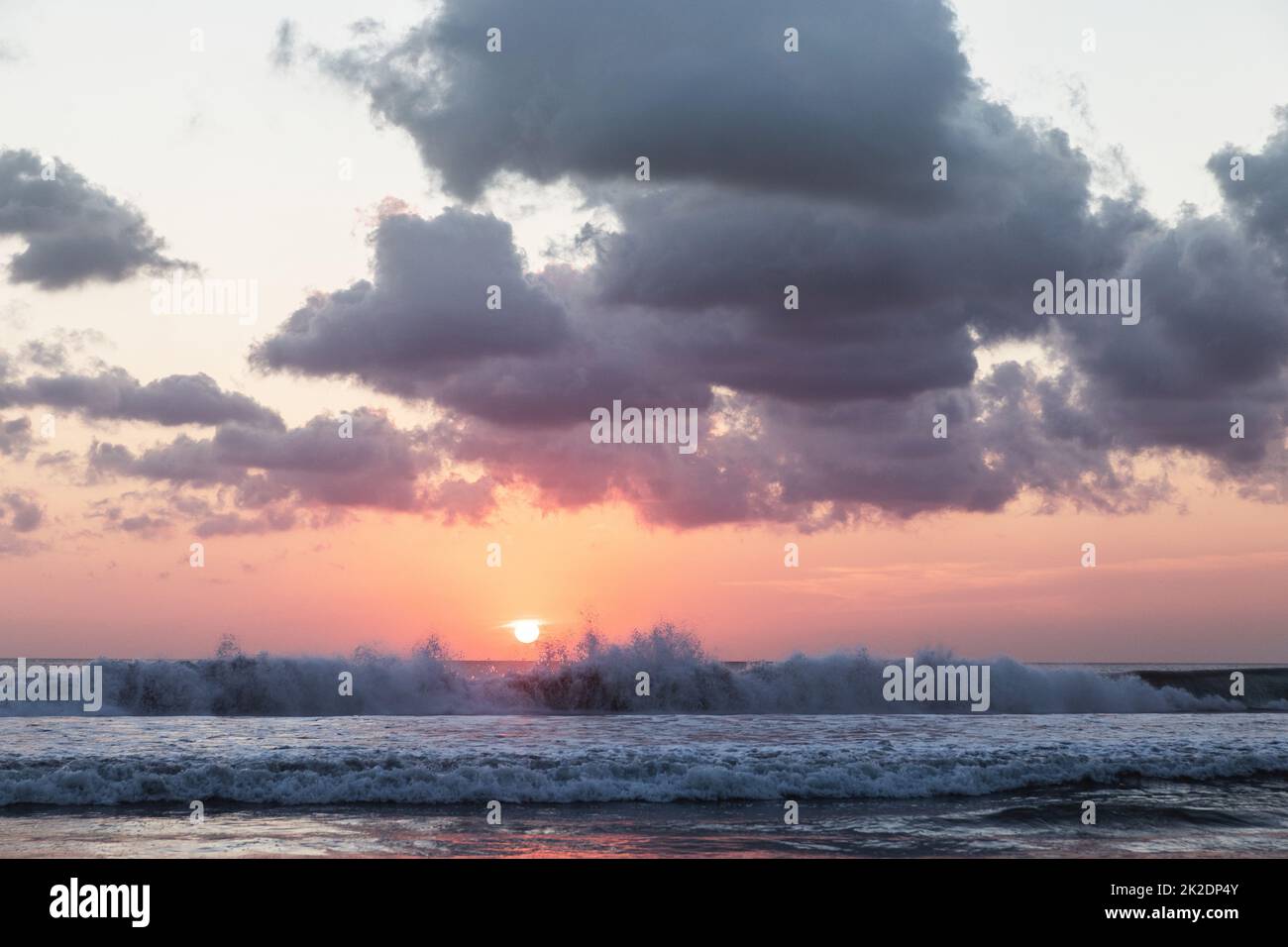 Sunset on the beach. Scenic seascape with clouds, waves and sun. Stock Photo