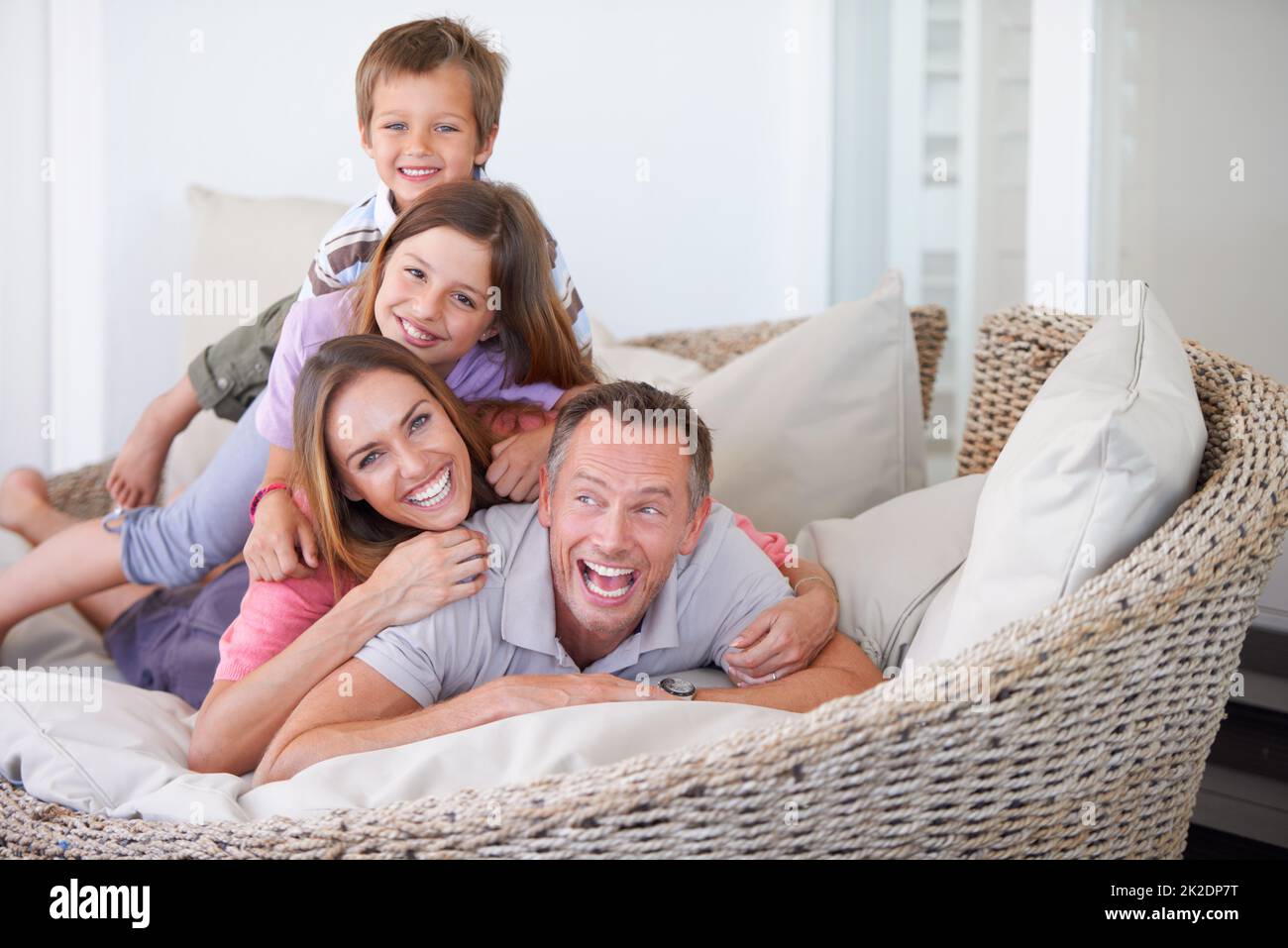 Pile on Dad. Portrait of a happy young family of four piled on top of one another. Stock Photo