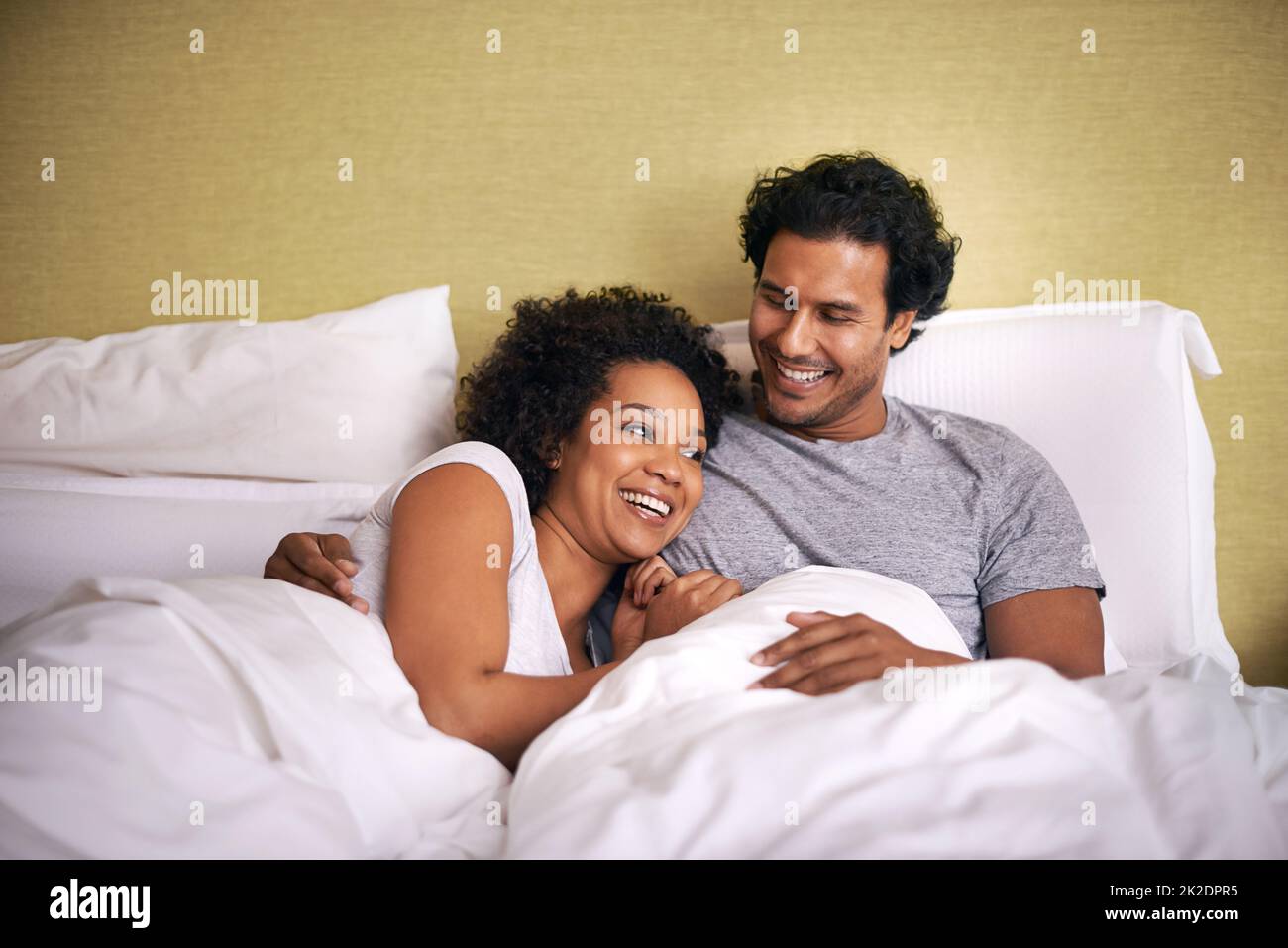 Enjoying a cuddle with the hubby. A young husband and wife lying bed together. Stock Photo