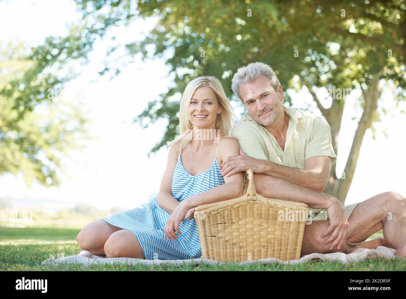 Picnic time in the park. A happy husband and wife sitting in a park with a picnic basket. Stock Photo