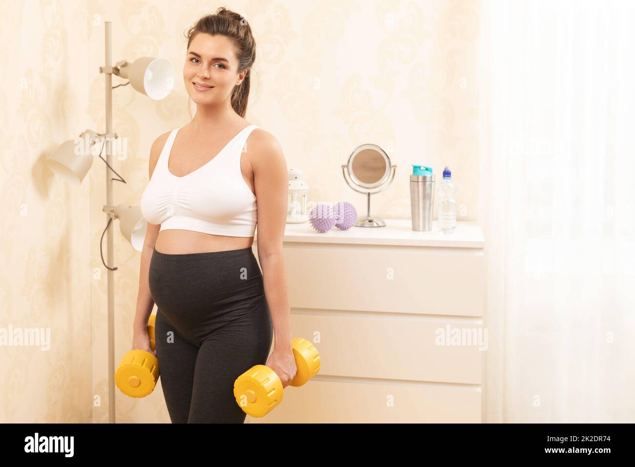 Pregnant woman during her fitness workout with yellow dumbbells at home Stock Photo