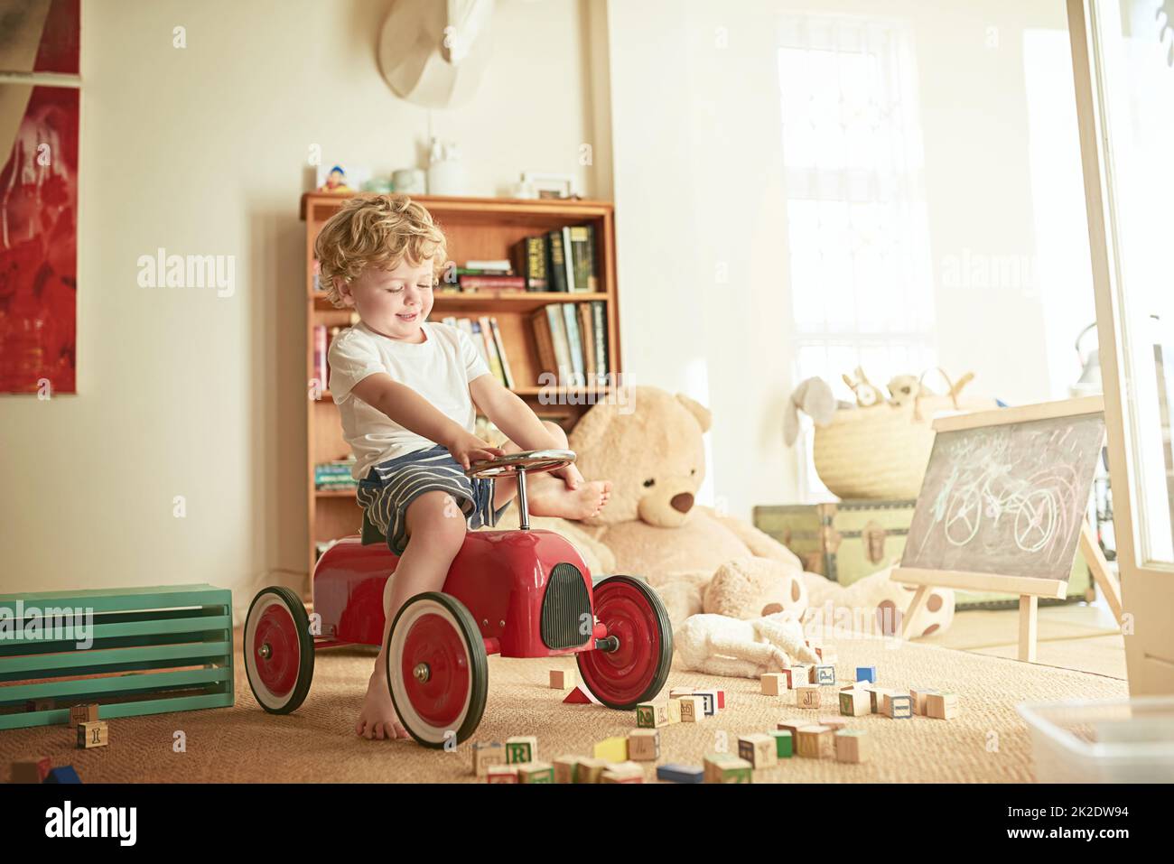 Imaginative play is essential to a childs development. Shot of a little boy playing on a toy car at home. Stock Photo