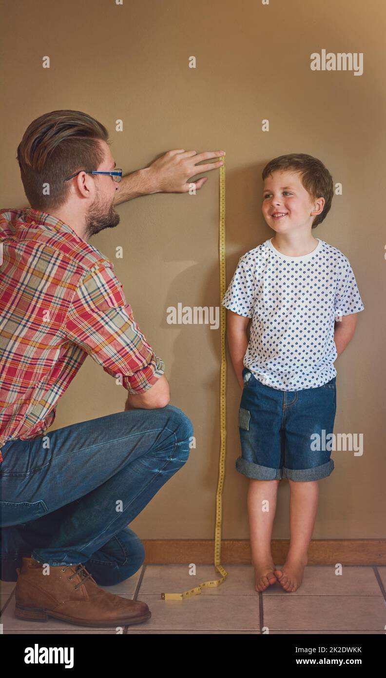 Look how much youve grown. Shot of a father measuring his little boys height against a wall at home. Stock Photo