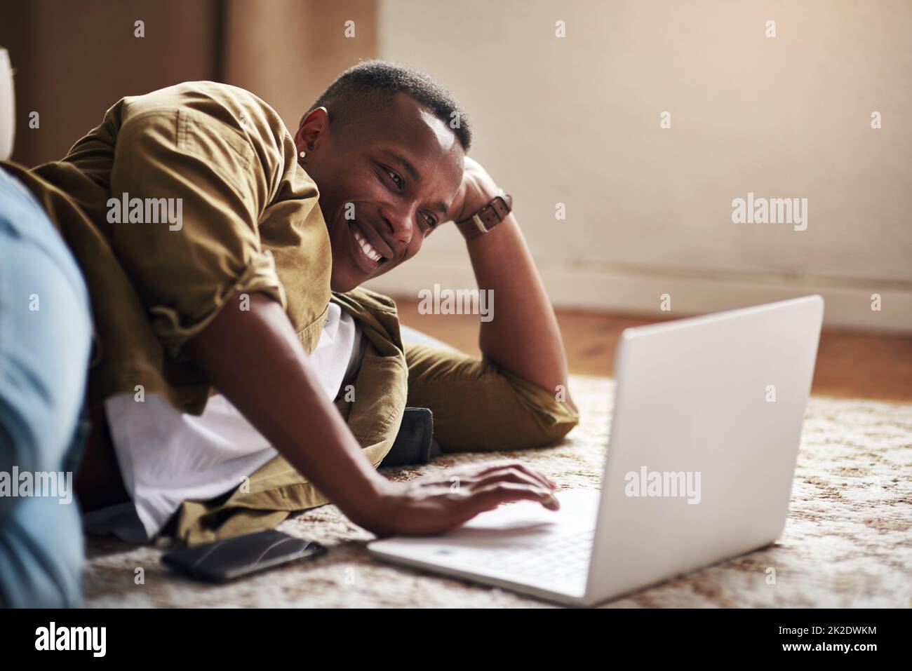 My blog has really reached a wide audience. Cropped shot of a handsome young man smiling while using a laptop in his living room at home. Stock Photo