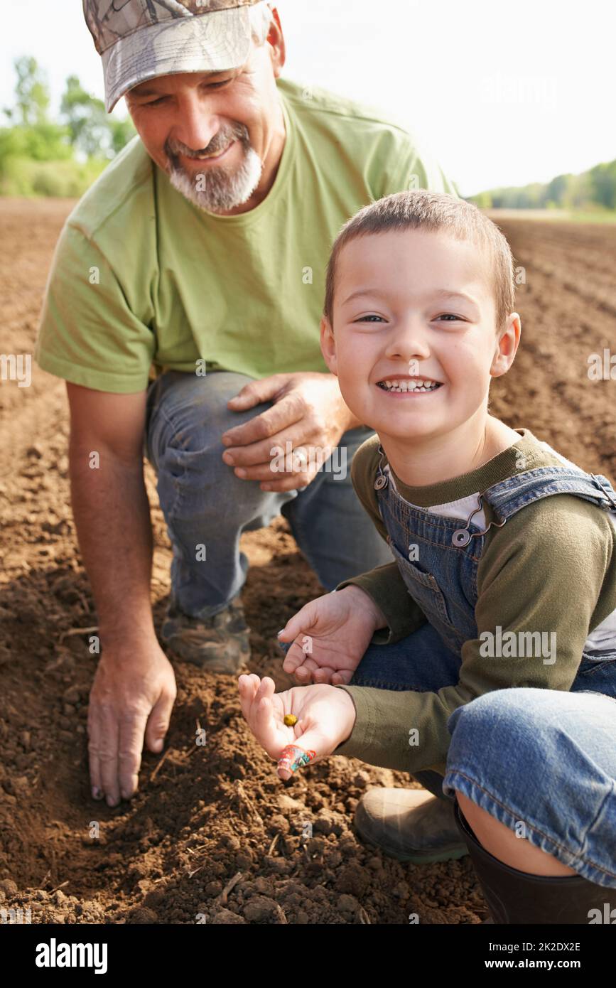 He loves getting his hands dirty. Portrait of a farmer and his son inspecting seeds in the ground. Stock Photo