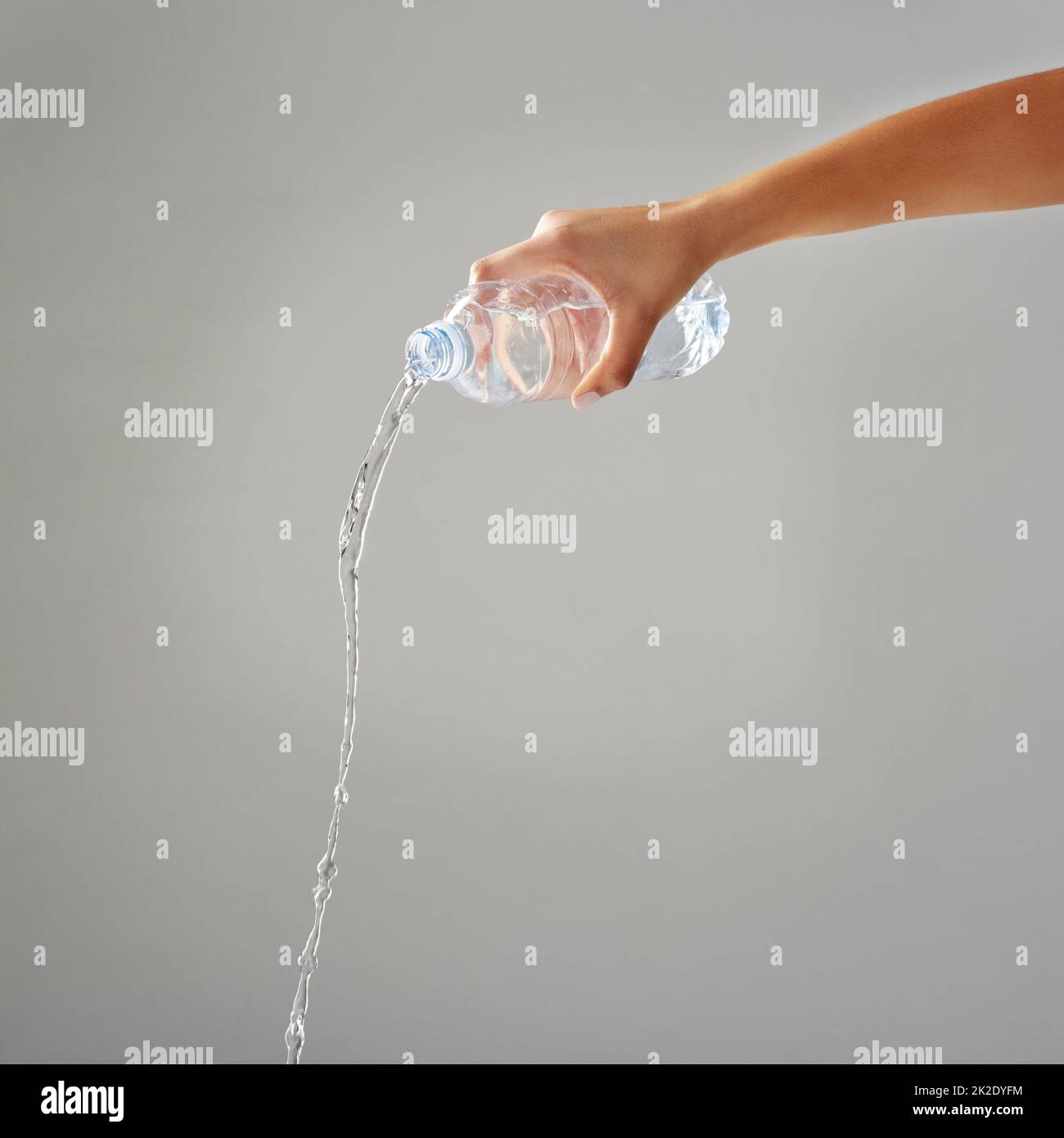 Purified water. Cropped shot of water being poured out of a bottle against a grey background. Stock Photo