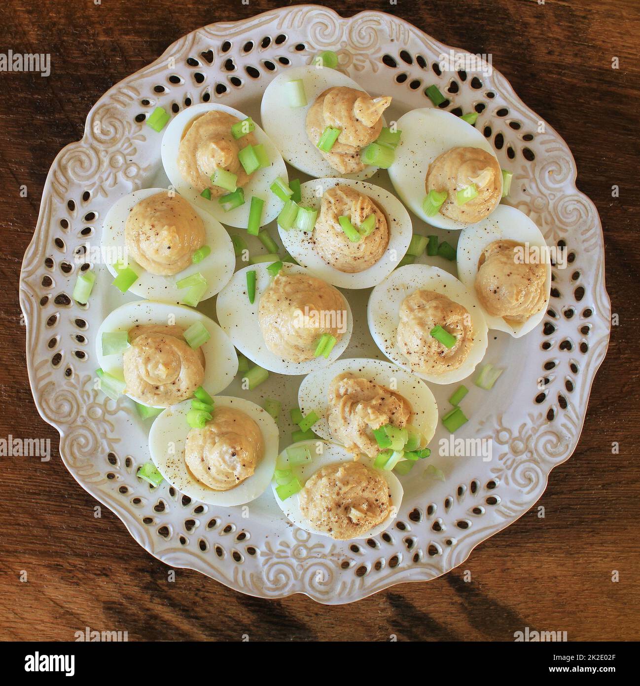Deviled eggs with cod livers with leek on white plate. Rustic wooden table Stock Photo