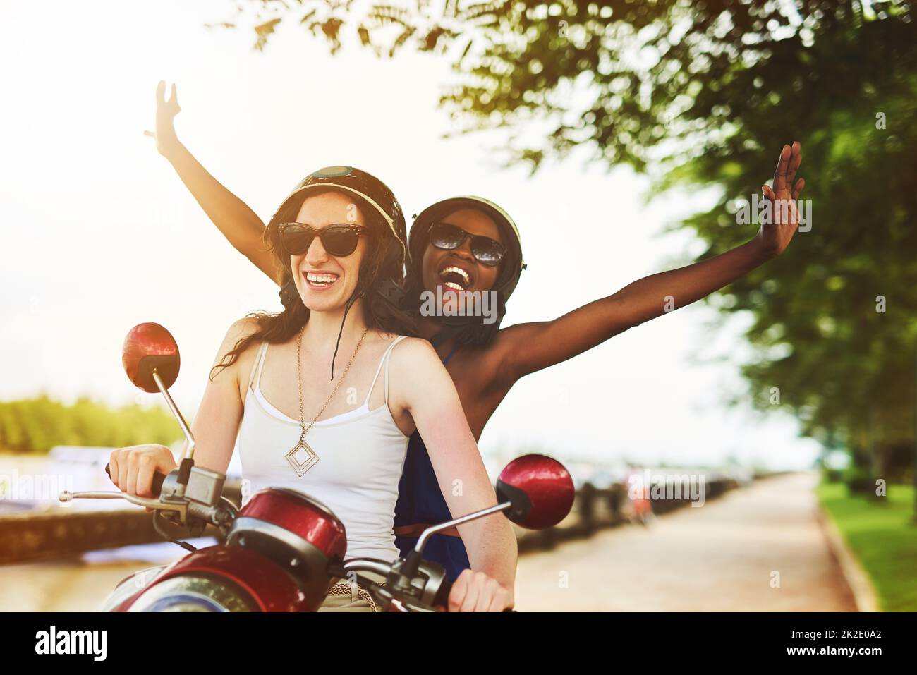 Loving the wind in their hair. Shot of two friends enjoying a ride on a scooter together. Stock Photo