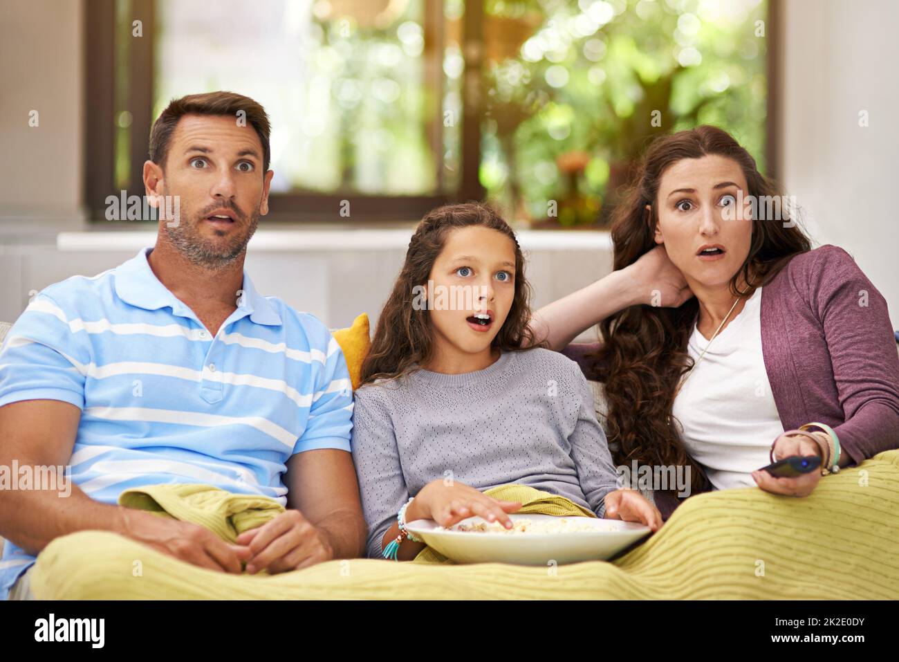 Absolutely shocked. Shot of a family sitting on their living room sofa watching a movie and eating popcorn. Stock Photo