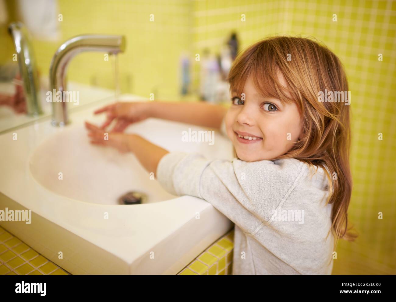 I can reach the tap now. A cute little girl washing her hands in the bathroom basin. Stock Photo