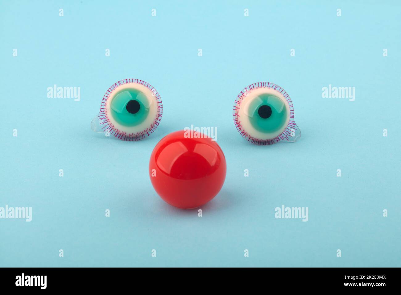 Decorative fruit candy eyes with red nose over light blue background. Conceptual photo using for funny celebration themes. Stock Photo