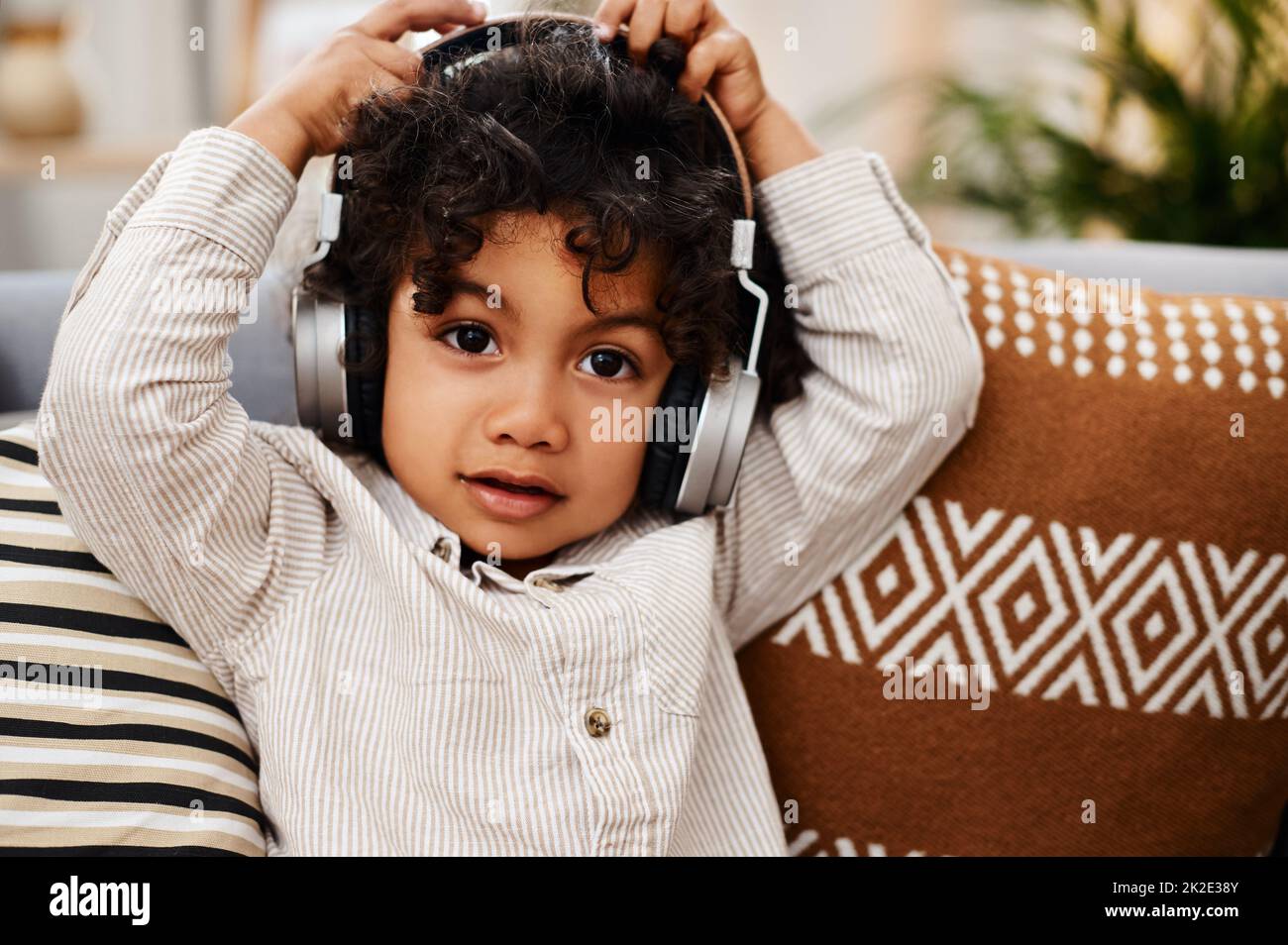 This song makes me lose my cool. Portrait of an adorable little boy listening to music on headphones while sitting on a sofa at home. Stock Photo