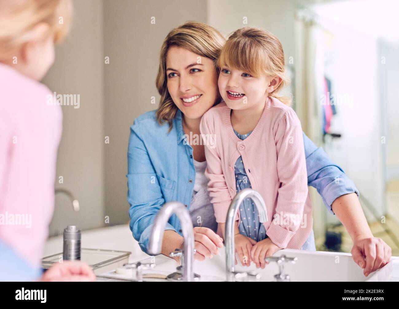 It can be fun indoors. Shot of a cheerful young mother and her daughter washing hands while looking at their reflection in a mirror. Stock Photo