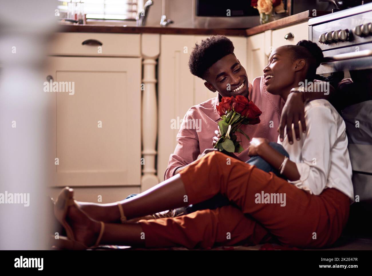 Every beautiful rose I see reminds me of you. Full length shot of an affectionate young man giving his wife a bunch of roses in their kitchen at home. Stock Photo