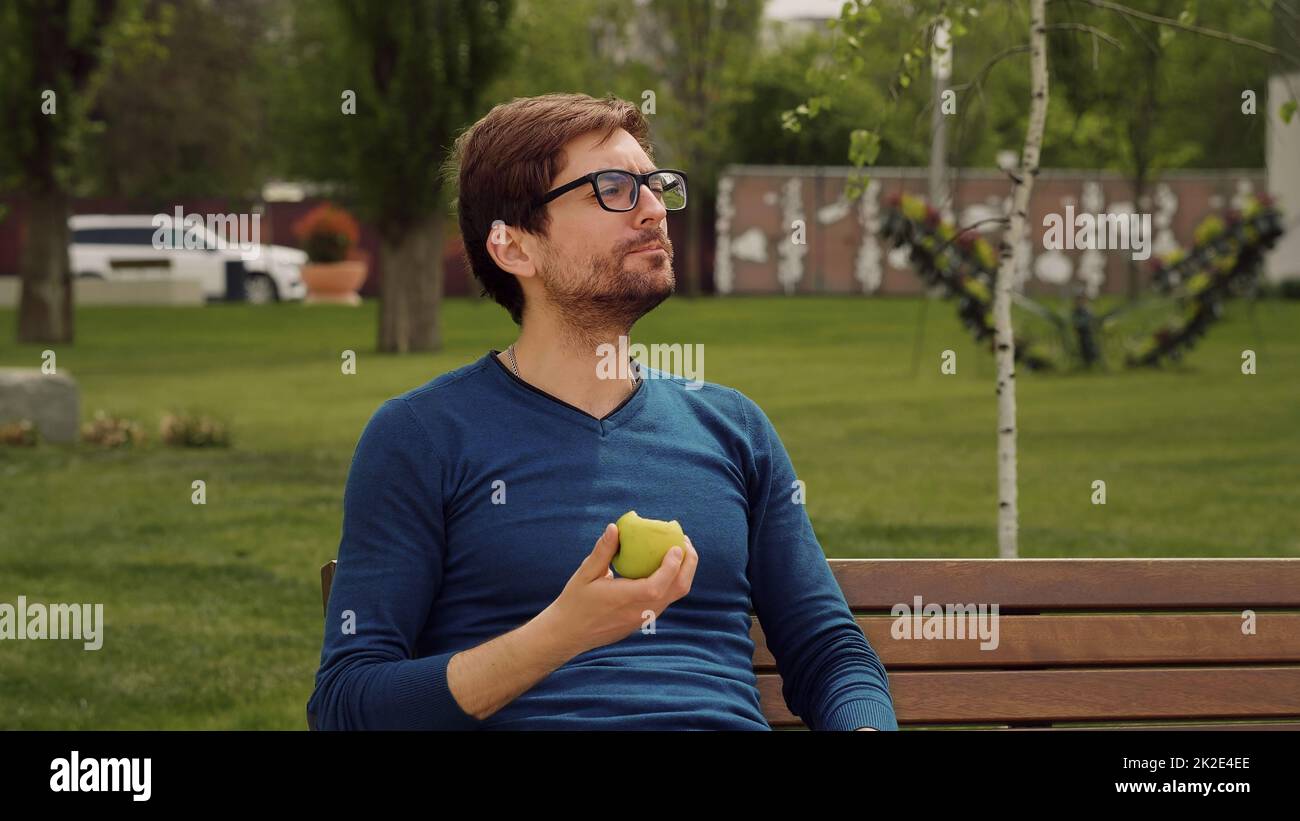 Handsome Man Eating Heathy food. Eating a apple as snack. Enjoying an fruit. Male Portrait have snack in park. Stock Photo