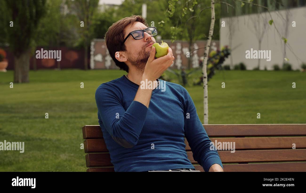 Young man Eating a apple as snack. Enjoying an fruit. Male Portrait have snack in park. Stock Photo