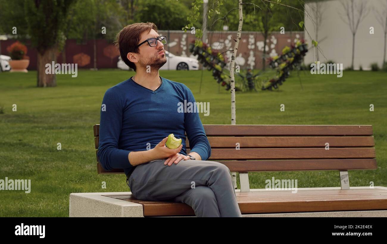 Handsome Man Eating Heathy food. Apple as Healthy Snack. Enjoying an fruit. Male Portrait have snack in park. Stock Photo