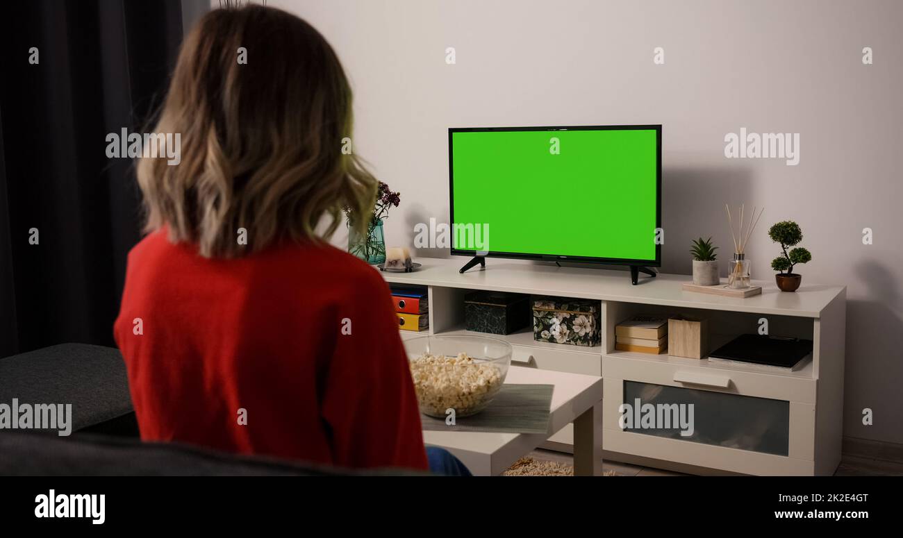 Woman watching TV focused eating popcorn. Green Screen TV Chroma Key. Movie time Sports Match, News, Sitcom TV Show in the evening. Stock Photo