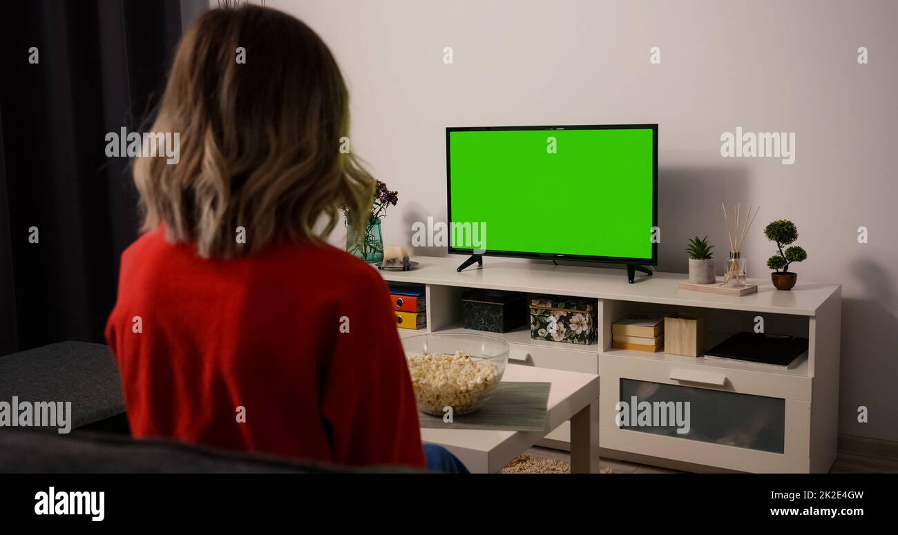 Woman watching TV focused eating popcorn. Green Screen TV Chroma Key. Stock Photo