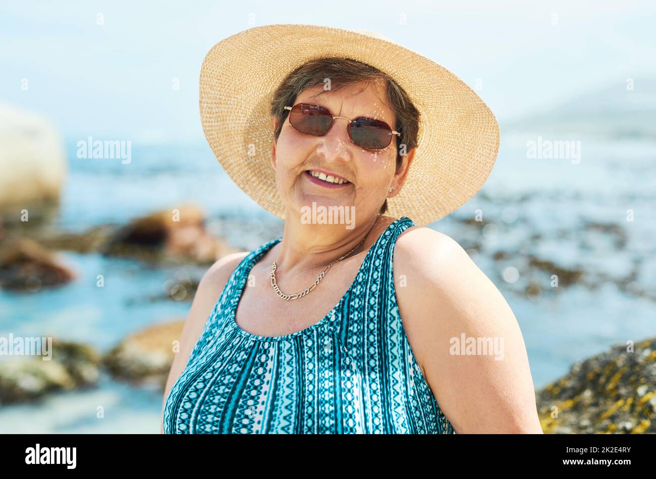 Time to get my tan on. Shot of an attractive mature woman standing alone during a day out on the beach. Stock Photo
