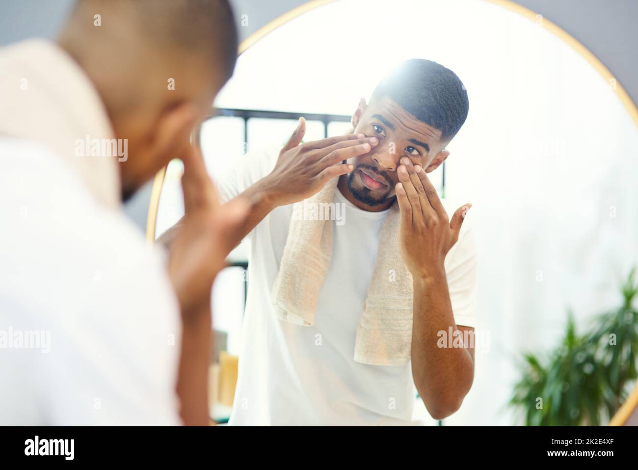 This face cream was well recommended. Young man applying face product in his bathroom mirror. Stock Photo