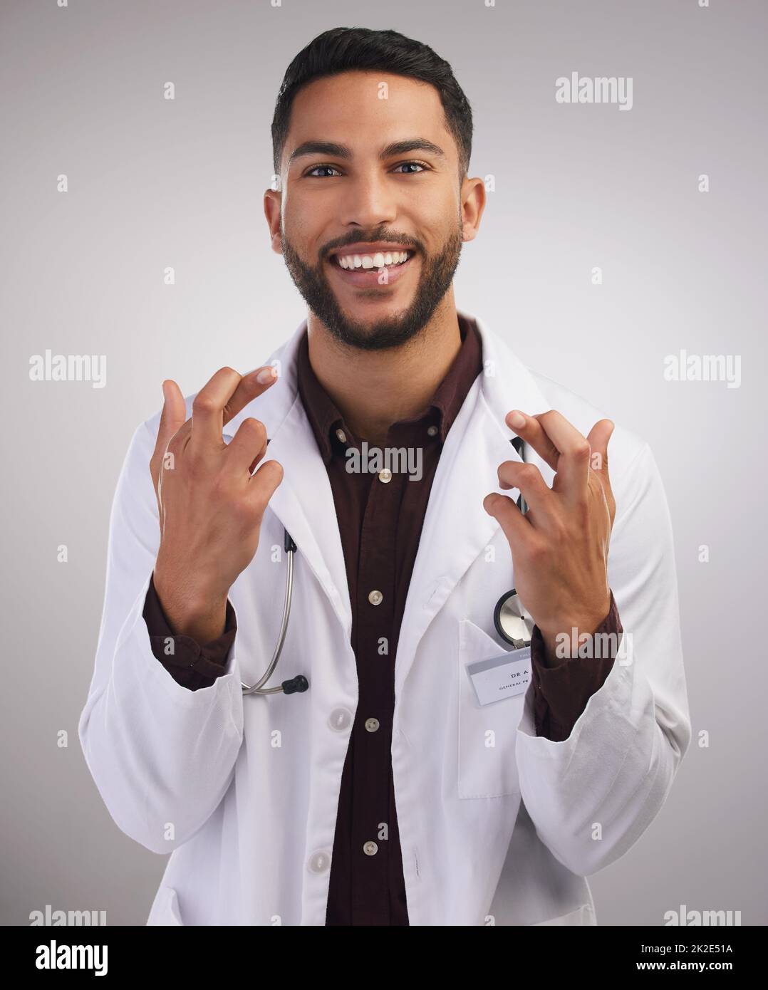 Well...fingers and toes are crossed. Shot of a handsome young doctor standing alone in the studio with his fingers crossed for good luck. Stock Photo